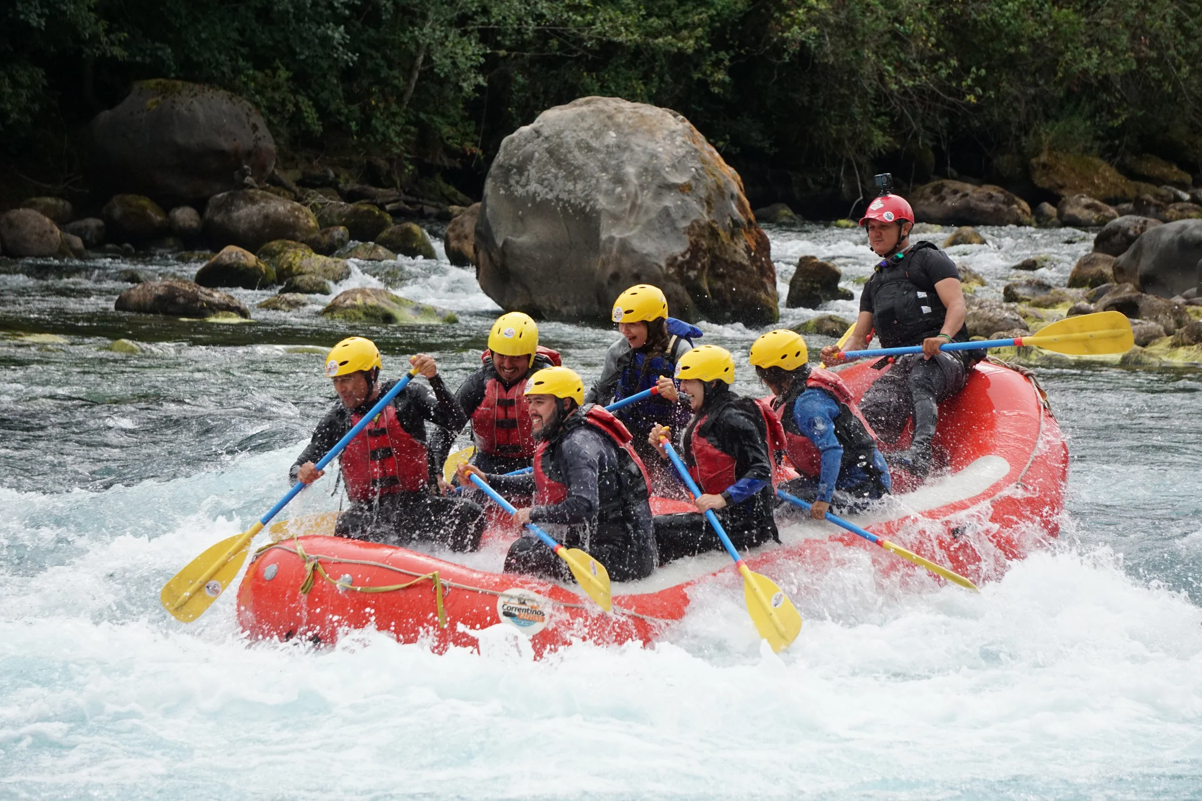 Grupo remando en un rápido junto a una gran roca